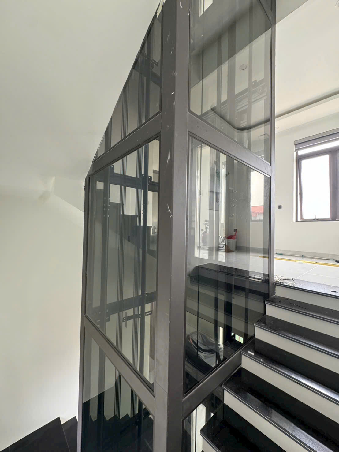 Thang máy kính gia đình lắp giữa cầu thang trong nhà hiện đại